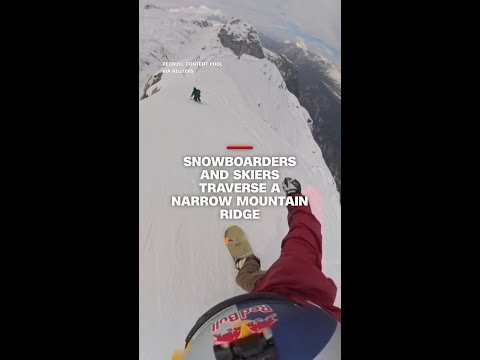 Snowboarders and skiers traverse a narrow mountain ridge