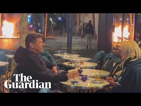 Couple enjoy a drink as fires burn nearby amid Paris unrest